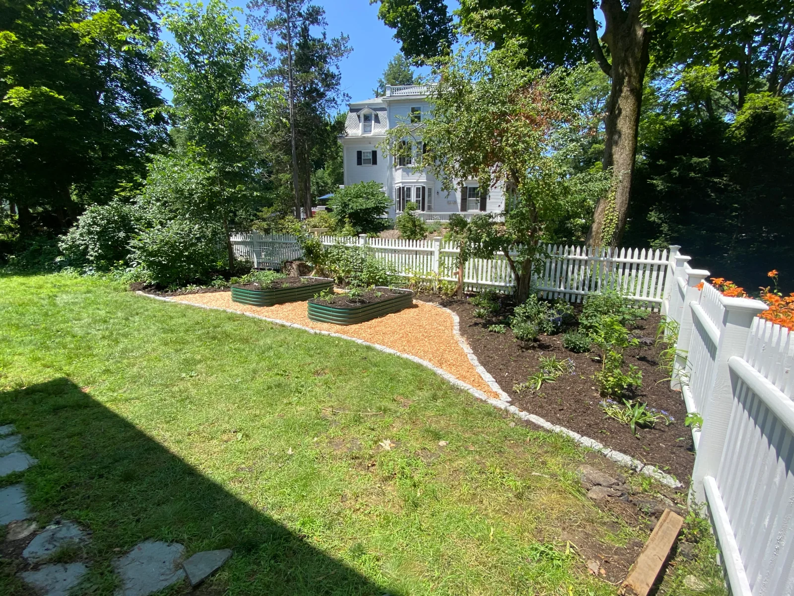 A mini food forest of layered edible and pollinator plantings behind a white picket fence